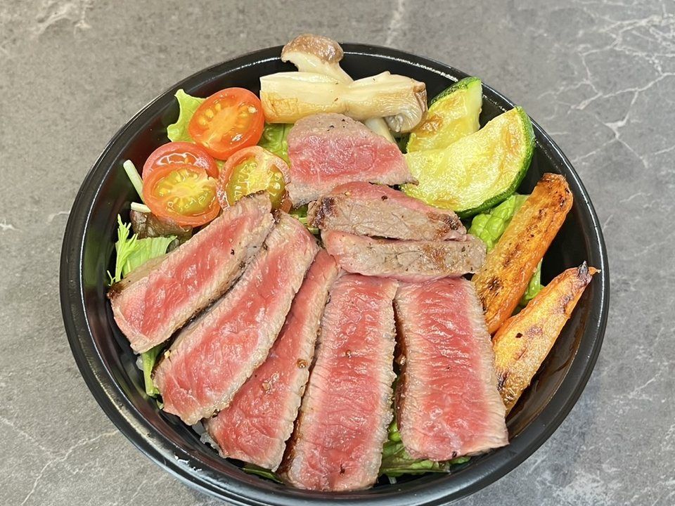 Wagyu beef bowl — sliced steak over rice with grilled vegetables and salad, in a black bowl